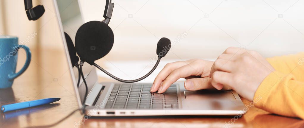 Laptop. headphones or headset on wooden desk and plain background. Female hands over laptop. Distant learning or working from home, online courses or support concept. Helpdesk or call center operator