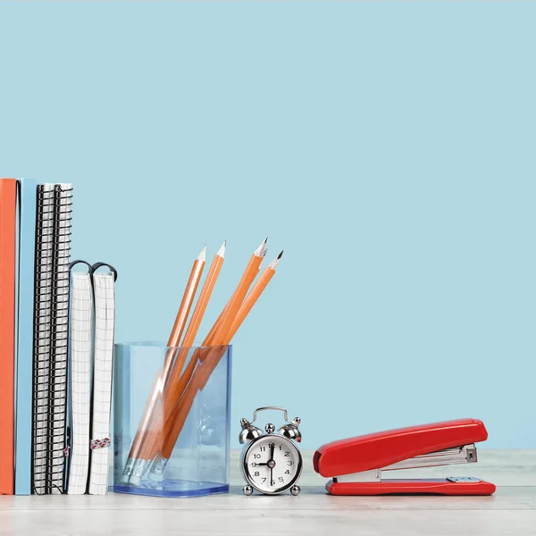 Organized office and school orange and pastel blue stationery, notebooks pencils scissors and alarm clock on grey wooden desk. Copy space for back to school education and craft concept