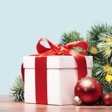 Kırmızı kurdeleli beyaz hediye kutusu Noel ağacı dalının yanında duruyor. Mırmır. Noel ve Yeni Yıl sınırı. Boşluk kenar görünümünü kopyala