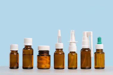 Bir sıra sahte ilaç hapları, kahverengi cam şişeler ve mavi arka planda burun spreyleri. Eczane ve reçeteli ilaçlar, grip mevsimi için ilaç. Boşluğu kopyala.