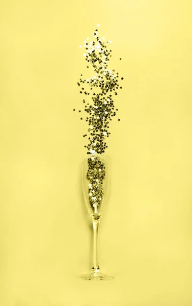 Glass with star-shaped confetti on yellow background. Stock Photo