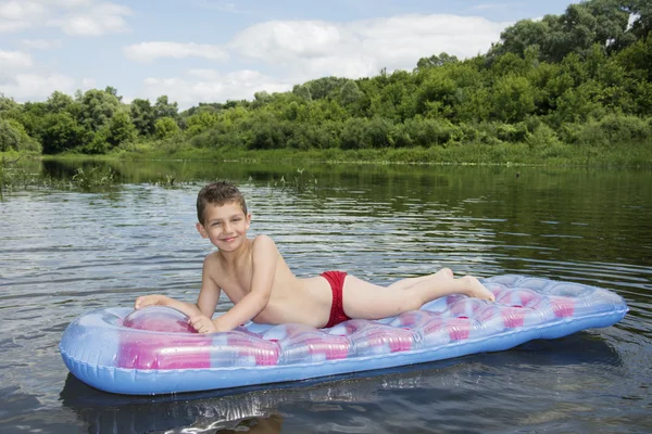 Summer on the river boy sits on an inflatable mattress on the ri — Stock Photo, Image