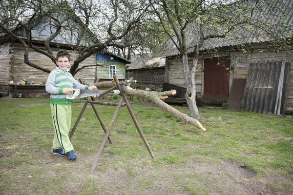 Våren i byn pojken sågning träd. — Stockfoto