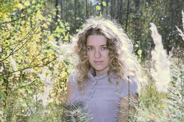 In the autumn forest on a glade curly girl in tall grass in the — Stock Photo, Image