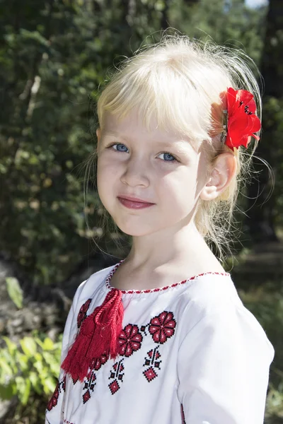 Die kleine Blondine mit den blauen Augen steht in der Stickerei im Wald — Stockfoto