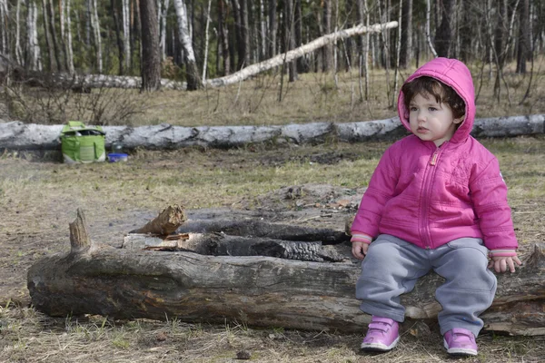 Klein meisje in de lente zit in het bos op een logboek. — Stockfoto