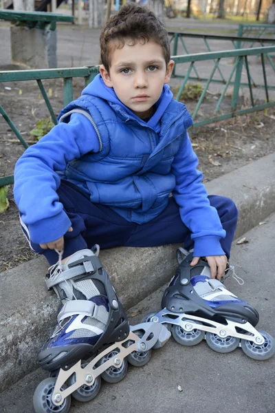 Sad little boy sits shod rollers on the curb. — Stock Photo, Image