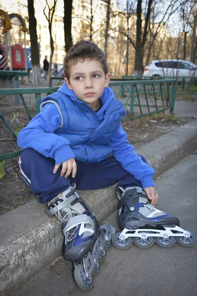 Trauriger kleiner Junge sitzt mit Rollschuhen auf dem Bordstein. — Stockfoto