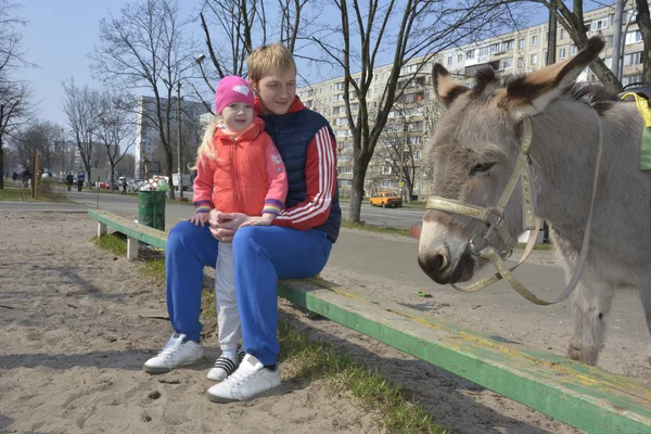 Chica con papá sentado al aire libre en un banco al lado de un puesto de burros — Foto de Stock