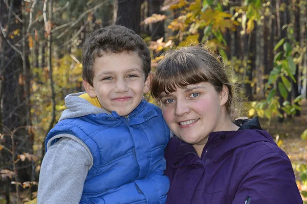 Mamá sostiene las manos de su hijo sonriente en el bosque otoñal . — Foto de Stock
