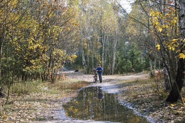 Otoño en el bosque un niño pequeño de pie con su bicicleta cerca — Foto de Stock