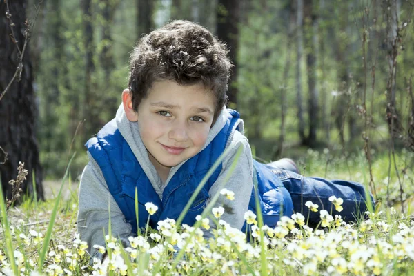 Frühling im Wald auf der Wiese liegt ein glücklicher Junge. — Stockfoto