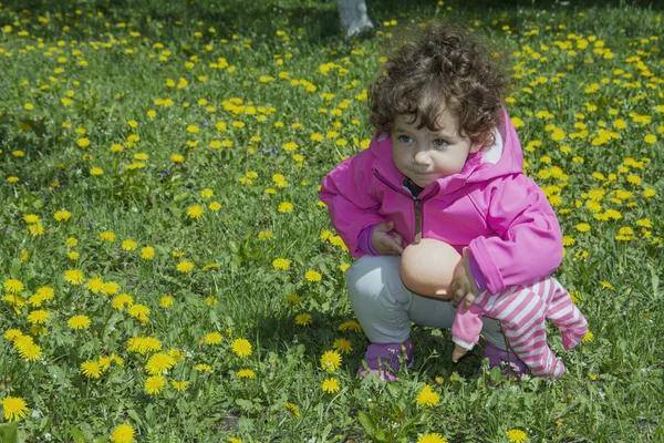 Kleines gelocktes Mädchen sitzt auf dem Feld in Löwenzahn. — Stockfoto