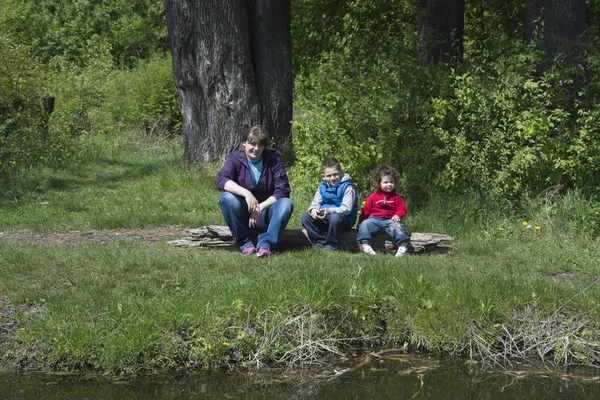 Spring on the shores of mother with children sitting on a log. — Stock Photo, Image