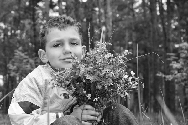 Black and white photo. The boy in the forest holding a bouquet o — Stock Photo, Image