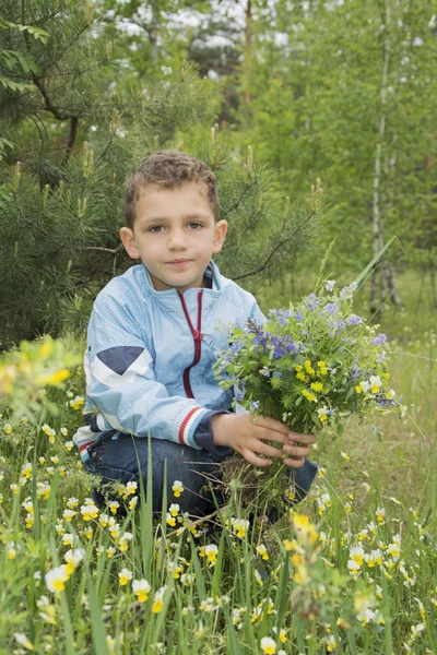 Le garçon dans la forêt tenant un bouquet de fleurs . — Photo