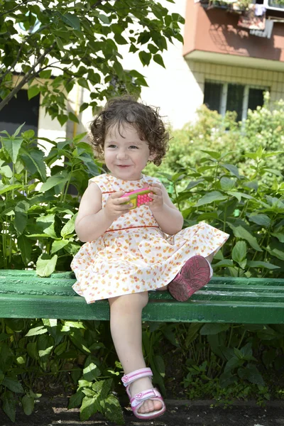 På sommaren sitter på bänken en liten flicka. — Stockfoto