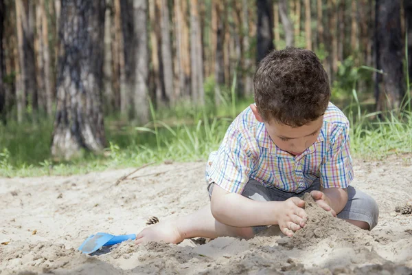 I sommaren i skogen lockigt pojken bygger ett hus av sand. — Stockfoto