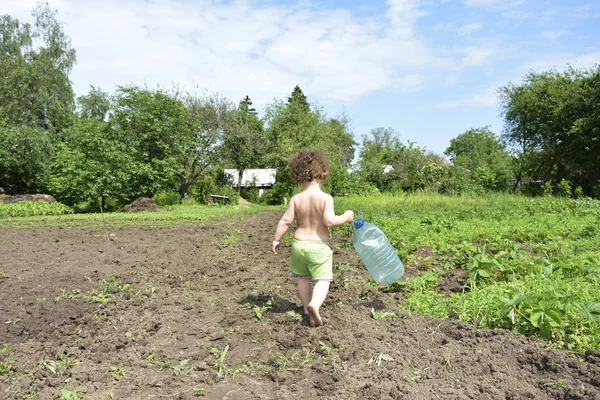 En verano, una pequeña chica rural rizada sosteniendo un gran bott de plástico — Foto de Stock