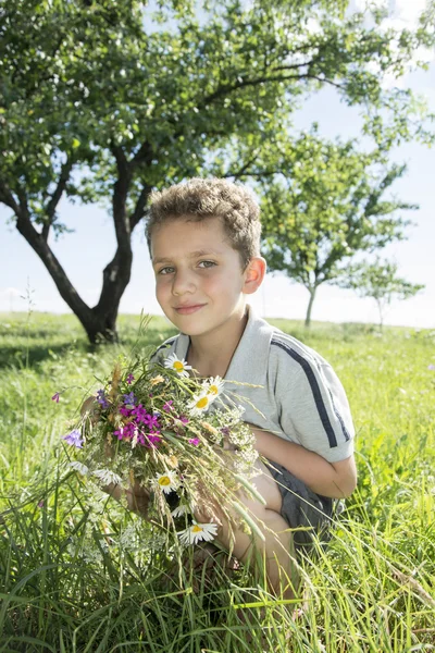 In estate, in giardino siede un piccolo ragazzo dalla testa riccia con un — Foto Stock