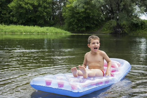 Verano en el niño del río se sienta en un colchón inflable en el río . — Foto de Stock