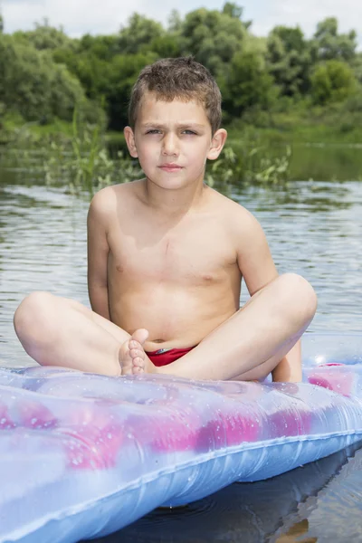 Summer on the river boy sits on an inflatable mattress on the ri — Stock Photo, Image