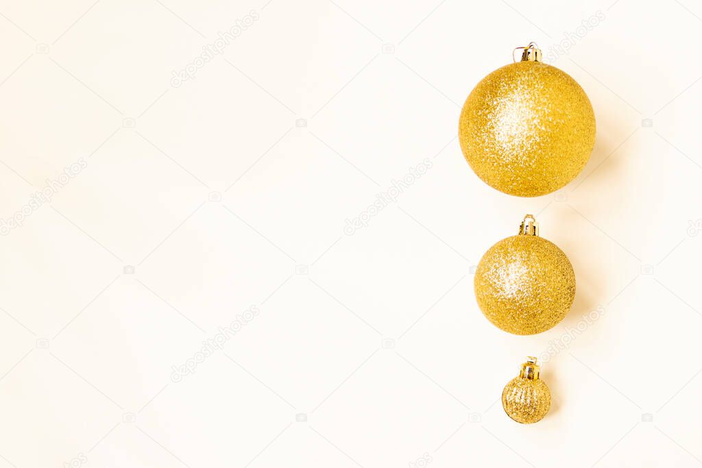 Three golden Christmas balls of different sizes are displayed in a row as a border on a white background. Copy space.