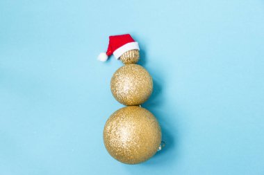 Mavi arka planda farklı boyutlarda altın noel toplarından yapılmış Noel kardan adamı. Kardan adamın üstünde kırmızı Noel Baba şapkası. Noel yaratıcısı. Boşluğu kopyala.