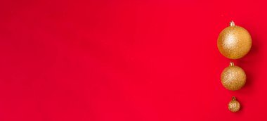 Farklı boyutlarda üç altın Noel topu arka planda kırmızı bir kenar olarak üst üste sergileniyor. Yeni yıl havası esiyor. Boşluğu kopyala.