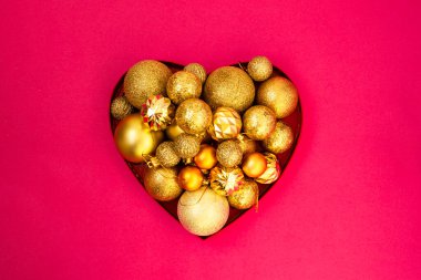 Noel yaratıcı minimalizmi. Altın parıltısı. Farklı boyutlarda Noel topları pembe arka planda kalp şeklinde bir kutuda toplanır. Düz yatış, üst görünüm