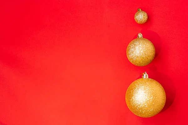 Drie gouden kerstballen van verschillende afmetingen worden op rij weergegeven als een rand op een rode achtergrond. Nieuwjaarsstemming. Kopieerruimte. — Stockfoto