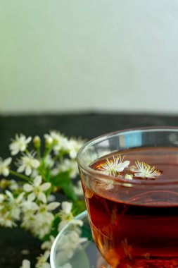 Bir fincan şeffaf çaydanlık çayı, çay tabağı ve siyah arka planda beyaz bir kiraz çiçeği. Uzayı kopyala Bahar kahvaltısı.