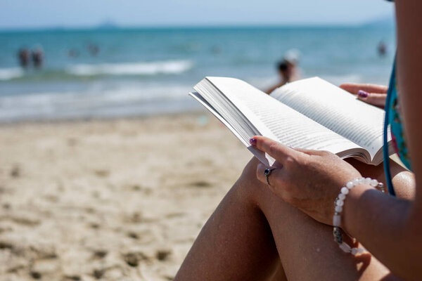 Woman reading a book on the beach, blurred background. Summer leisure on the beach.