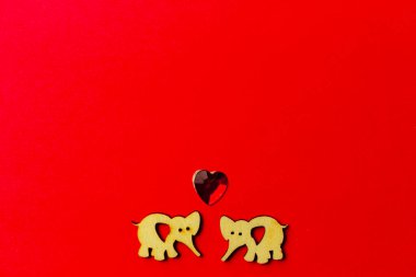 Kırmızı zemin üzerinde kristal bir kalbi olan iki ahşap fil. Uzayı kopyala Sevgililer günü ve düğün. Aşk kartpostalı