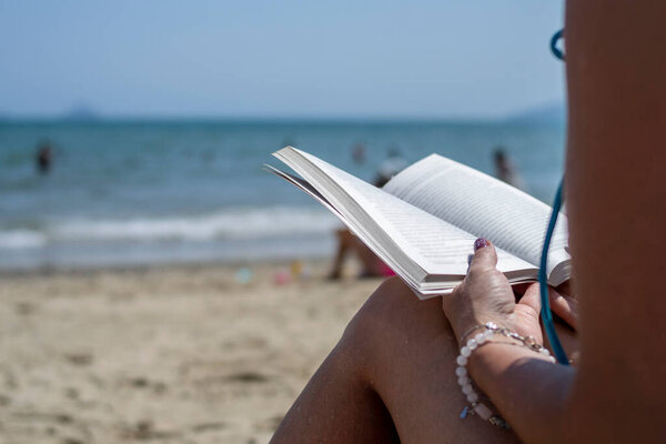 Woman reading a book on the beach, blurred background. Summer leisure on the beach.