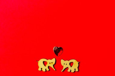Kırmızı zemin üzerinde kristal bir kalbi olan iki ahşap fil. Uzayı kopyala Sevgililer günü ve düğün. Aşk kartpostalı