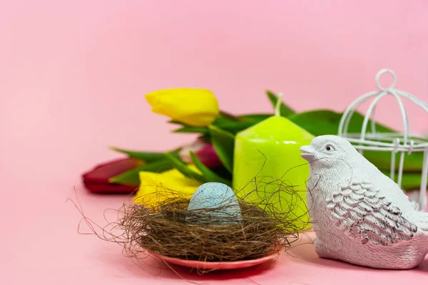 Spring postcard. Easter eggs in a nest with moss, a bird, a cage and a bouquet of fresh tulips, a green candle on a pink background. Easter concept. Flat top view copy space. Spring flowers tulips