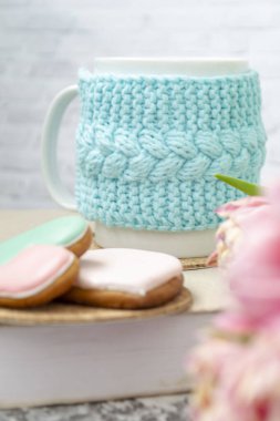 Örülmüş mavi bir çantanın içinde beyaz bir fincan çay bir kitap, pembe çiçekler, laleler ve dokuma masasındaki zencefilli ekmeğin üzerinde duruyor. Bahar konsepti.