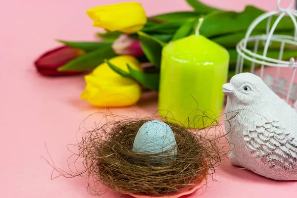Spring postcard. Easter eggs in a nest with moss, a bird, a cage and a bouquet of fresh tulips, a green candle on a pink background. Easter concept. Flat top view copy space. Spring flowers tulips