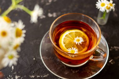 Siyah arka planda şeffaf bir fincanda limonlu papatya çayı. Kahvaltı konsepti, bitki çayı.