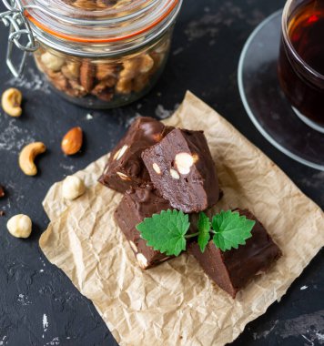 Nane yapraklarıyla süslenmiş ev yapımı çikolatalı şekerleme ve siyah arka planda çay ile servis ediliyor. Arka plandaki fındıklar bulanık. Boşluğu kopyala