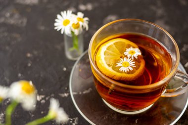 Siyah arka planda şeffaf bir fincanda limonlu papatya çayı. Kahvaltı konsepti, bitki çayı.