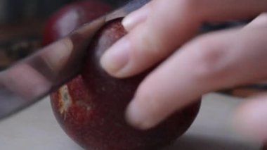 Bir kadının elinin yakın çekimi kırmızı bir çarkıfelek meyvesini ortada bir bıçakla keser ve sarı bir dolguyu ortaya çıkarır.