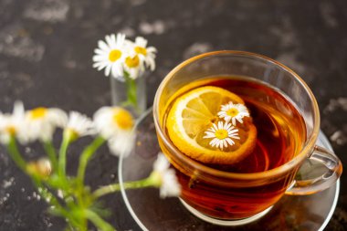 Siyah arka planda şeffaf bir fincanda limonlu papatya çayı. Kahvaltı konsepti, bitki çayı.