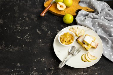 Beyaz bir tabakta dilimlenmiş turta ve siyah bir masada armut reçeli. Arka plandaki yeşil armutlar bulanık. Sabah kahvaltısı.