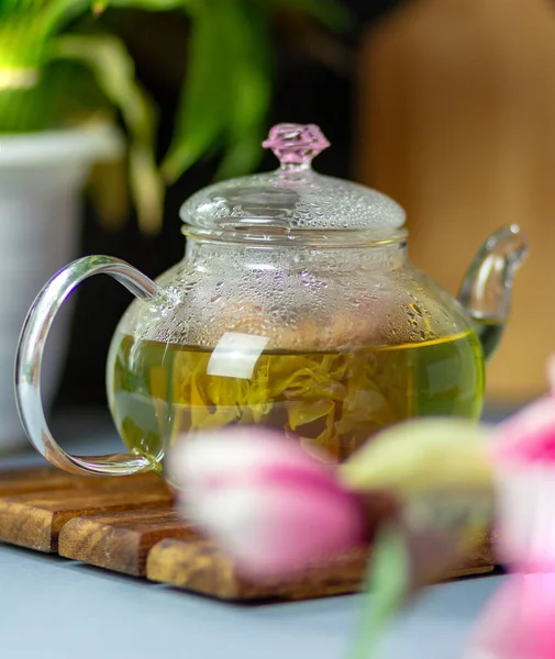 green tea with rose petals in a transparent teapot on a wooden table on a black background. The background is blurred. Tea drinking