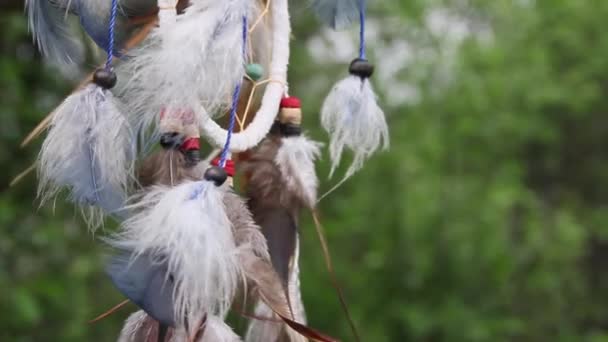 Un atrapasueños con plumas multicolores revolotea en el viento contra el telón de fondo de la vegetación borrosa de la naturaleza. Concepto de relajación. — Vídeo de stock