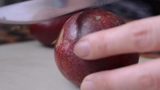 Close-up of a womans hand cuts a red passionfruit with a knife in the middle, and reveals a yellow filling. — Stock Video