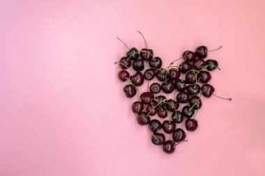 Pembe arka planda kalp şeklinde kırmızı kirazlar. Kiraz arkaplanı. Pembe arka planda izole edilmiş tatlı kiraz. Boşluğu kopyala.