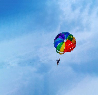 İki adam mavi gökyüzüne karşı renkli ve parlak bir paraşütle yelken açıyorlar. Boşluğu kopyala
